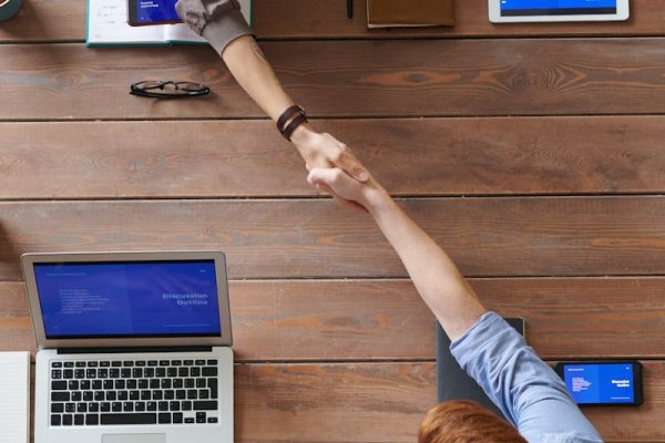 Overhead view of colleagues in a work meeting using laptops and tablets, emphasizing teamwork and technology.
